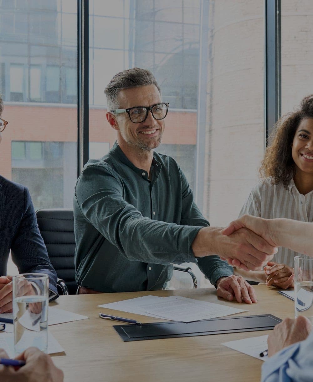 Two people shaking hands across a meeting table